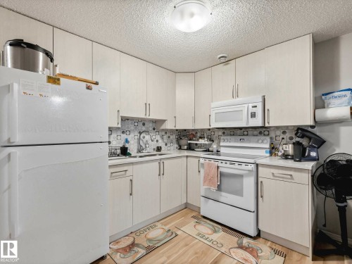 Kitchen featuring white cabinetry, white appliances, a patterned tile backsplash, light wood-finish flooring, and a flush-mount ceiling light - 2435 12 Avenue, Edmonton, AB - Indoor Photo Showing Kitchen