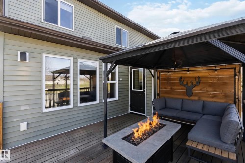 Outdoor living area featuring a covered gazebo, built-in fire pit, wood panel accent wall, string lighting, and direct access to the interior - 1825 Westerra Loop, Stony Plain, AB - Outdoor With Deck Patio Veranda With Exterior