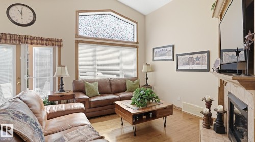 Living area featuring vaulted ceilings, wood-finish flooring, and a fireplace with a stone surround - 5 Richelieu Place, Beaumont, AB - Indoor Photo Showing Living Room