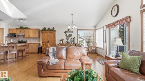 Vaulted ceiling great room featuring wood-finish flooring, a kitchen with light wood cabinetry, a dining area, multiple windows, and a glass-paneled door - 5 Richelieu Place, Beaumont, AB - Indoor Photo Showing Living Room