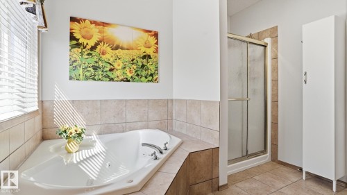 Corner soaking tub with tile surround, adjacent to a window with blinds - 5 Richelieu Place, Beaumont, AB - Indoor Photo Showing Bathroom