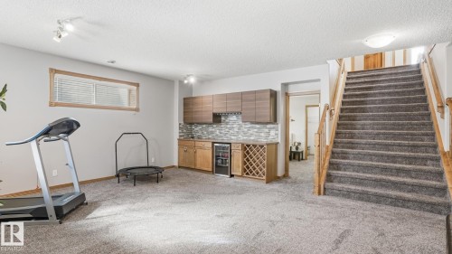 Finished basement featuring a built-in wet bar with wood-finish cabinetry, tile backsplash, and wine storage - 5 Richelieu Place, Beaumont, AB - Indoor