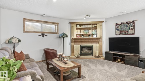 Corner fireplace with a tile surround and mantel, flanked by built-in shelving and cabinetry - 5 Richelieu Place, Beaumont, AB - Indoor Photo Showing Living Room With Fireplace