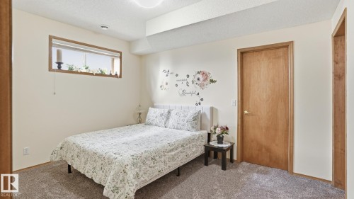 Carpeted room featuring a horizontal window with wood trim, light beige walls, and a solid wood door with brushed nickel hardware - 5 Richelieu Place, Beaumont, AB - Indoor Photo Showing Bedroom
