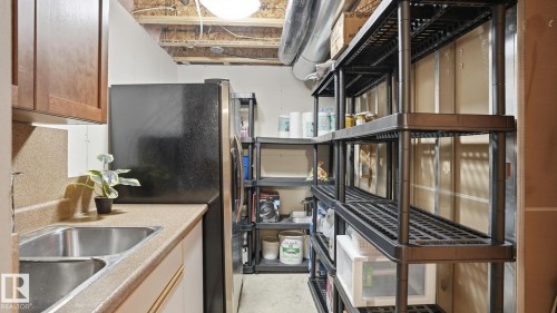 Utility space featuring a double-basin stainless steel sink, wood-finish upper cabinetry, and ample shelving for storage - 5 Richelieu Place, Beaumont, AB - Indoor Photo Showing Kitchen With Double Sink