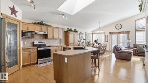Open-concept living area featuring a kitchen with light wood cabinetry, stainless steel appliances, and a central island with a sink - 5 Richelieu Place, Beaumont, AB - Indoor Photo Showing Kitchen