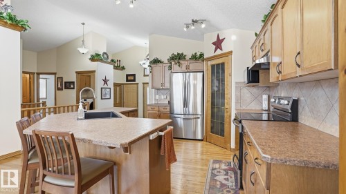 Kitchen featuring a large island with an integrated sink, wood-finish flooring, stainless steel appliances, light wood cabinetry, and a tile backsplash - 5 Richelieu Place, Beaumont, AB - Indoor Photo Showing Kitchen