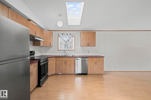 Kitchen featuring wood-finish cabinetry, stainless steel appliances, a corner sink with window, and a skylight - 623 Evergreen Park, Edmonton, AB - Indoor Photo Showing Kitchen With Double Sink