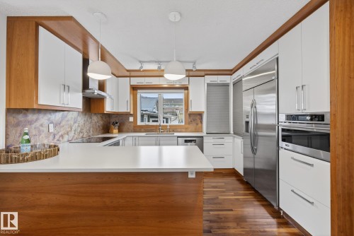 The kitchen features white cabinetry complemented by wood accents, a window above the sink, stainless steel appliances, and pendant lighting - 9736 78 Avenue, Edmonton, AB - Indoor Photo Showing Kitchen With Upgraded Kitchen