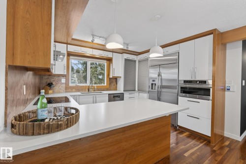 The kitchen features a spacious island with a white countertop, wood cabinetry, and stainless steel appliances - 9736 78 Avenue, Edmonton, AB - Indoor Photo Showing Kitchen