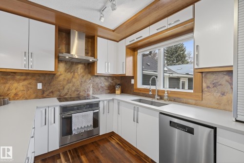 The kitchen features white cabinetry, stainless steel appliances including a range hood and oven, and rich wood flooring - 9736 78 Avenue, Edmonton, AB - Indoor Photo Showing Kitchen