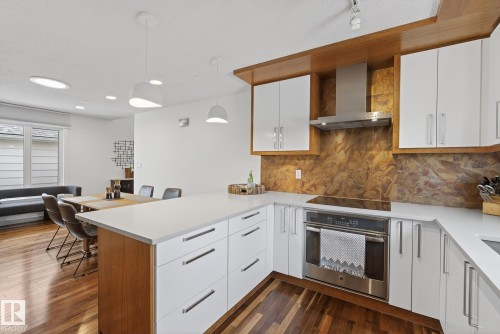 The kitchen features white cabinetry with sleek hardware, light countertops, and a built-in oven with a stainless steel range hood - 9736 78 Avenue, Edmonton, AB - Indoor Photo Showing Kitchen With Upgraded Kitchen
