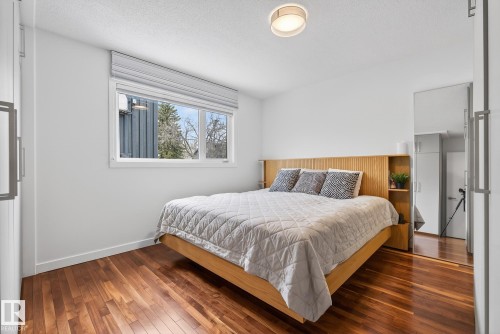 This room features rich hardwood flooring, a large window with a modern blind, and a contemporary ceiling light fixture - 9736 78 Avenue, Edmonton, AB - Indoor Photo Showing Bedroom