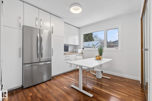 This bright space features extensive white cabinetry, a stainless steel refrigerator, and rich hardwood flooring - 9736 78 Avenue, Edmonton, AB - Indoor Photo Showing Kitchen