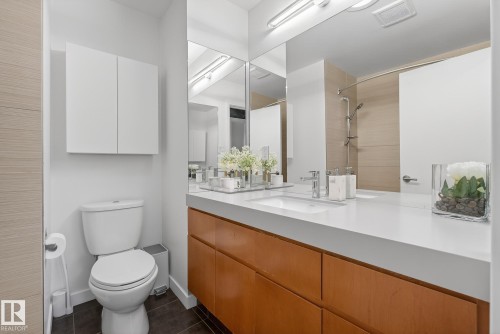 The bathroom features a white vanity with an integrated sink and a large mirror, a toilet, and a shower with a sliding door and tiled wall - 9736 78 Avenue, Edmonton, AB - Indoor Photo Showing Bathroom