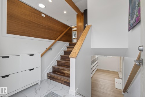 Entryway featuring a wooden staircase with a natural wood handrail, recessed lighting, and a partial view of a lower level with light wood flooring - 9736 78 Avenue, Edmonton, AB - Indoor Photo Showing Other Room