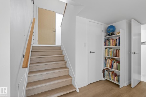 The property features a staircase with light-toned wooden treads and a wooden handrail, complemented by white walls - 9736 78 Avenue, Edmonton, AB - Indoor Photo Showing Other Room