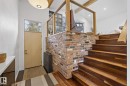 Entryway featuring a light-colored door with an overhead transom window, a prominent exposed brick wall, and rich wood stairs with a matching wood railing - 9736 78 Avenue, Edmonton, AB  - Indoor Photo Showing Other Room 