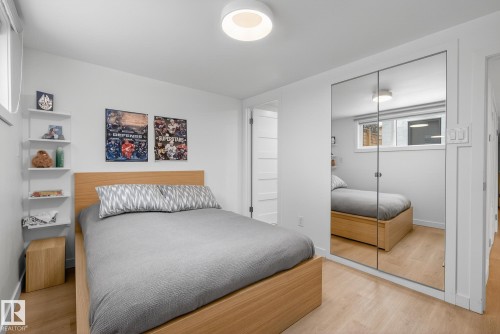 This room features light hardwood flooring, a window with roller blinds, and a contemporary ceiling light fixture - 9736 78 Avenue, Edmonton, AB - Indoor Photo Showing Bedroom