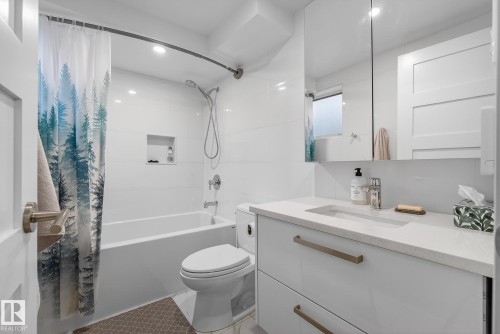 Bathroom featuring white subway tile, a bathtub with shower, a modern vanity with an integrated sink, and an illuminated mirror - 9736 78 Avenue, Edmonton, AB - Indoor Photo Showing Bathroom
