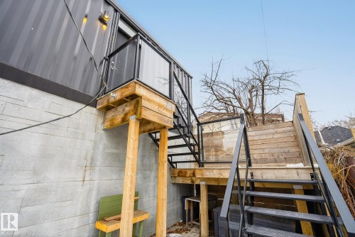 The property features an exterior staircase with dark metal handrails and wooden treads, alongside a raised wooden landing with glass panel railings - 9736 78 Avenue, Edmonton, AB - Outdoor