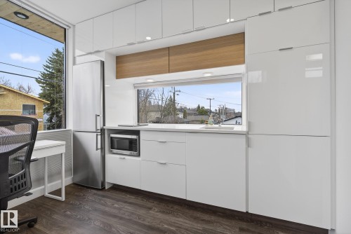 The kitchen features sleek white cabinetry, a stainless steel refrigerator, and a built-in microwave - 9736 78 Avenue, Edmonton, AB - Indoor Photo Showing Kitchen