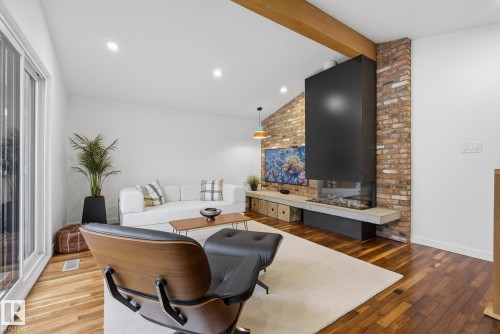 Living area featuring hardwood flooring, a modern fireplace with a black hood and brick surround, and a vaulted ceiling with a visible wooden beam - 9736 78 Avenue, Edmonton, AB - Indoor