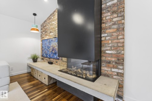 Living area featuring a modern fireplace with a glass enclosure, hardwood floors, and a brick accent wall - 9736 78 Avenue, Edmonton, AB - Indoor Photo Showing Other Room