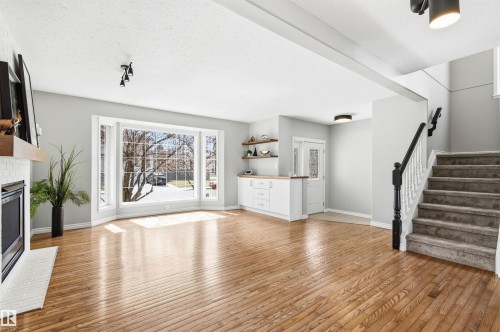 Spacious living area featuring polished wood-finish flooring, a white brick fireplace with a wood mantle, and a large bay window - 8730 92A Avenue, Edmonton, AB - Indoor Photo Showing Living Room