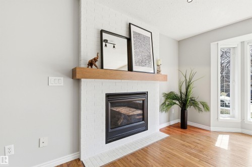 White brick fireplace featuring a warm wood mantel and a black-framed insert - 8730 92A Avenue, Edmonton, AB - Indoor Photo Showing Living Room With Fireplace