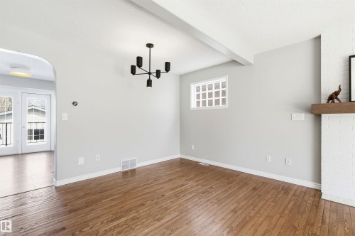 Hardwood flooring extending throughout, complemented by a white painted brick fireplace with a wood mantel - 8730 92A Avenue, Edmonton, AB - Indoor Photo Showing Other Room