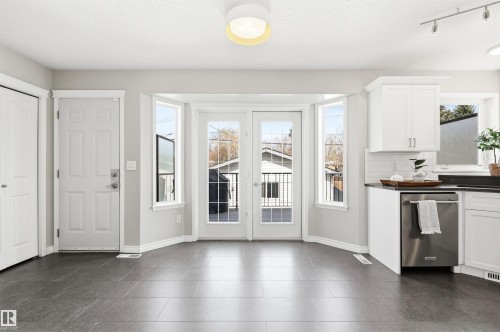 Open-concept space featuring dark tile flooring, white shaker-style cabinetry, and a stainless steel dishwasher - 8730 92A Avenue, Edmonton, AB - Indoor Photo Showing Kitchen