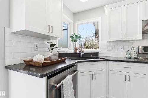 Corner kitchen sink with a stainless steel faucet, dark countertop, white subway tile backsplash, white shaker-style cabinetry, and stainless steel dishwasher - 8730 92A Avenue, Edmonton, AB - Indoor Photo Showing Kitchen With Double Sink