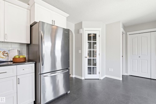 Kitchen area featuring white shaker-style cabinetry with chrome hardware, a stainless steel refrigerator, and dark countertops - 8730 92A Avenue, Edmonton, AB - Indoor Photo Showing Kitchen