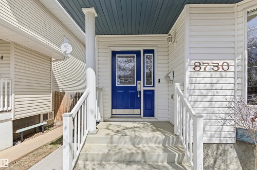 Front entry featuring a bright blue door with decorative glass inserts, white siding, and concrete steps - 8730 92A Avenue, Edmonton, AB - Outdoor With Exterior