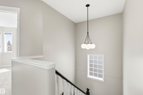 Stairwell featuring a contemporary chandelier with five spherical lights, a prominent window with privacy glass, white trim, and a black handrail with white spindles - 8730 92A Avenue, Edmonton, AB - Indoor Photo Showing Other Room