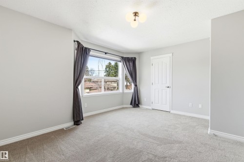 Carpeted room featuring a bay window, light gray walls, white trim, and a three-bulb ceiling light fixture - 8730 92A Avenue, Edmonton, AB - Indoor Photo Showing Other Room