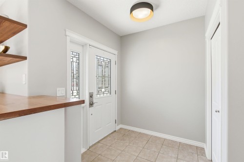 Entryway featuring a white door with decorative glass inserts, ceramic tile flooring, a built-in wood-finish shelf system, and a modern ceiling light fixture - 8730 92A Avenue, Edmonton, AB - Indoor Photo Showing Other Room