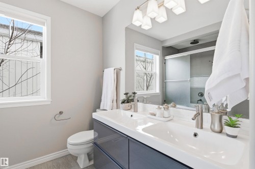 Bathroom featuring a dual-sink vanity with a white countertop and blue-gray cabinetry, a toilet, and a shower/tub combination with sliding glass doors - 8730 92A Avenue, Edmonton, AB - Indoor Photo Showing Bathroom