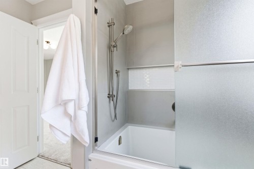 Bathtub and shower combination featuring a tiled surround, integrated shelf with mosaic accent tile, and a handheld shower fixture - 8730 92A Avenue, Edmonton, AB - Indoor