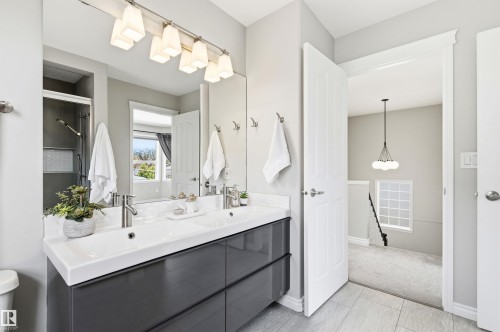 Spacious bathroom featuring a dual-sink vanity with dark cabinetry, integrated white countertops, and brushed nickel fixtures - 8730 92A Avenue, Edmonton, AB - Indoor Photo Showing Bathroom