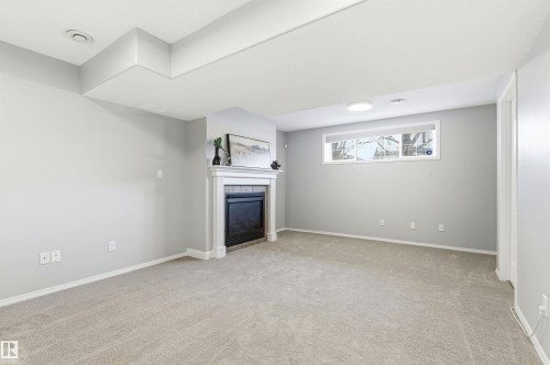 Spacious room featuring a white-mantled fireplace, neutral gray walls, light-toned carpeting, and a window providing natural light - 8730 92A Avenue, Edmonton, AB - Indoor Photo Showing Other Room