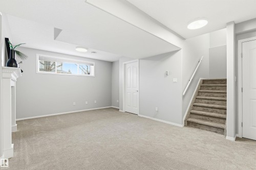 Finished basement living area featuring neutral carpeting, a white mantel, and a horizontal window - 8730 92A Avenue, Edmonton, AB - Indoor