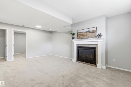 Living area featuring a gas fireplace with a tiled surround and white mantel, light gray walls, and neutral carpeting - 8730 92A Avenue, Edmonton, AB - Indoor With Fireplace