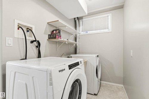 Dedicated laundry area featuring a window with blinds, tile flooring, and integrated wall shelving - 8730 92A Avenue, Edmonton, AB - Indoor Photo Showing Laundry Room