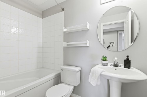 Bathroom featuring a white pedestal sink, a round wall-mounted mirror, and a white toilet - 8730 92A Avenue, Edmonton, AB - Indoor Photo Showing Bathroom