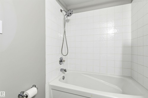 Tub and shower combination featuring white square tile surround, chrome fixtures, a handheld showerhead, and a integrated tub - 8730 92A Avenue, Edmonton, AB - Indoor Photo Showing Bathroom