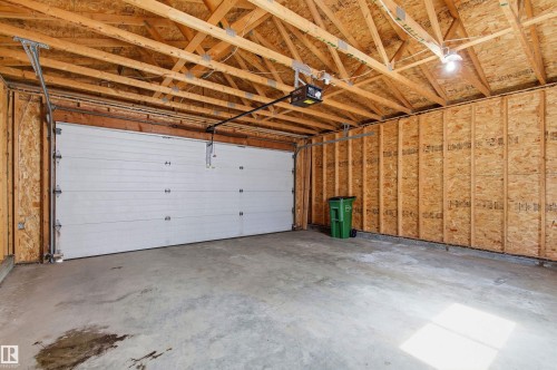 Attached garage featuring an automatic overhead door, exposed wooden ceiling trusses, concrete flooring, and unfinished wood panel walls - 8730 92A Avenue, Edmonton, AB - Indoor Photo Showing Garage
