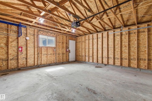 Spacious garage featuring exposed wood truss ceiling, integrated garage door opener, concrete flooring, and a single window for natural light - 8730 92A Avenue, Edmonton, AB - Indoor Photo Showing Basement