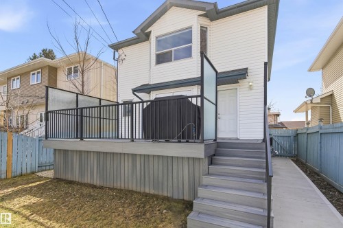 Rear exterior featuring white horizontal siding, a composite deck with black metal railings and privacy screens, and exterior lighting - 8730 92A Avenue, Edmonton, AB - Outdoor With Exterior
